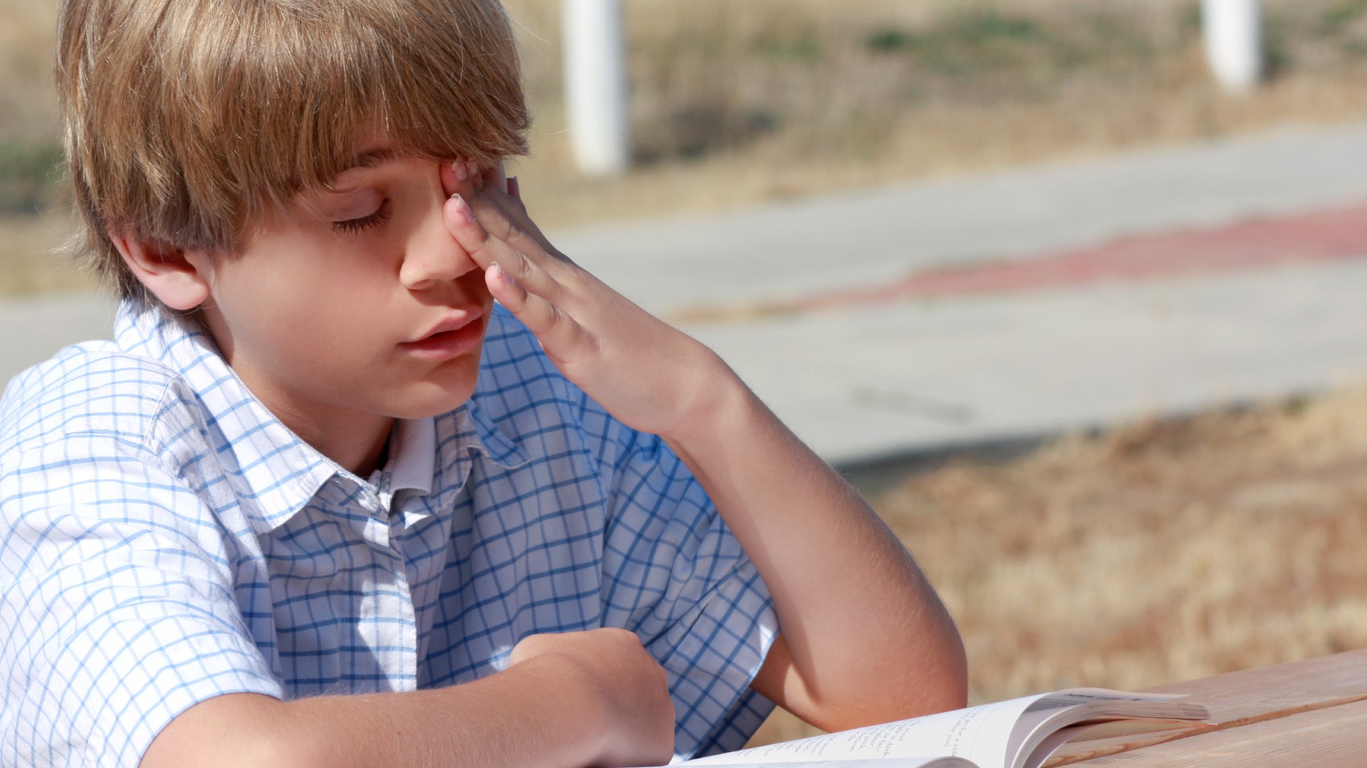 Adolescente muy aburrido en una mesa exterior tratando de leer.  J. McPhail a través de Shutterstock