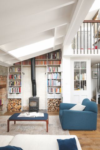 bookshelves surrounding stove, sloped ceiling, white walls, wooden flooring, large rug, blue sofa