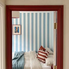 bedroom with blue and white striped wall, red woodwork and red striped cushions on the bed