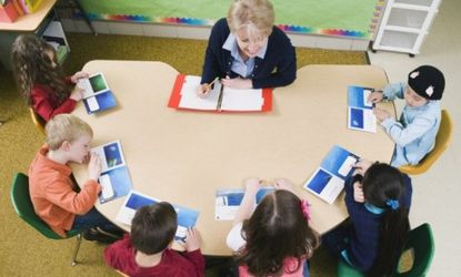 Kindergarten students sit at a table with their teacher: Using smiley, neutral, and sad faces to indicate grades, Georgia's five-year-olds will soon be tasked with evaluating their teachers' 
