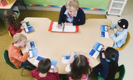 Kindergarten students sit at a table with their teacher: Using smiley, neutral, and sad faces to indicate grades, Georgia&amp;#039;s five-year-olds will soon be tasked with evaluating their teachers&amp;#039; 