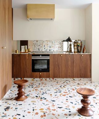 colors that go with brown, brown kitchen with wood veneer cabinetry, terrazzo tiles on floor, wooden stools, mirrored backsplash, cooker hood, cream walls