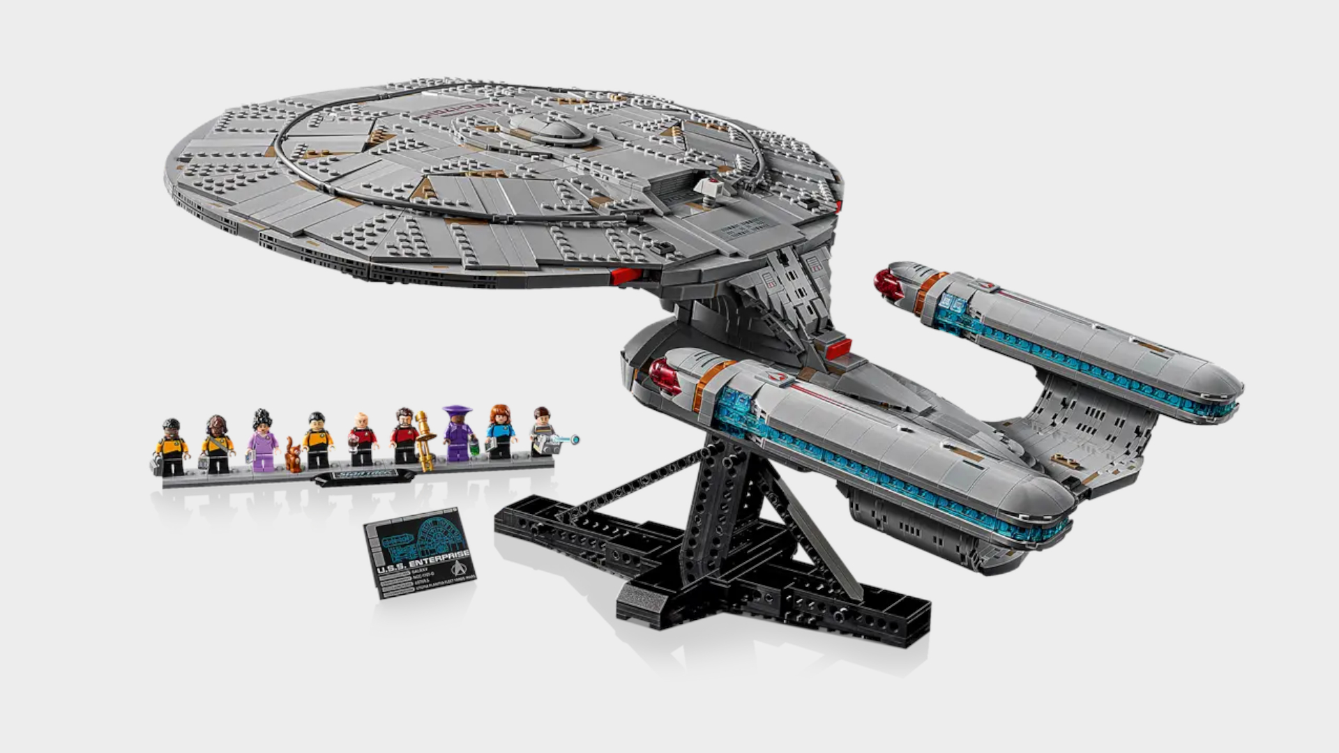 Lego Enterprise on stand in front of minifigures, all against a plain background