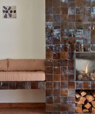 chocolate brown glossy zellige tiled fireplace with connected bench seat with striped upholstery and stacked logs