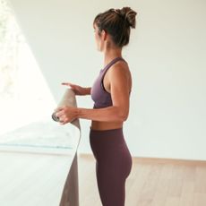 A woman rolling up a Pilates mat in workout gear