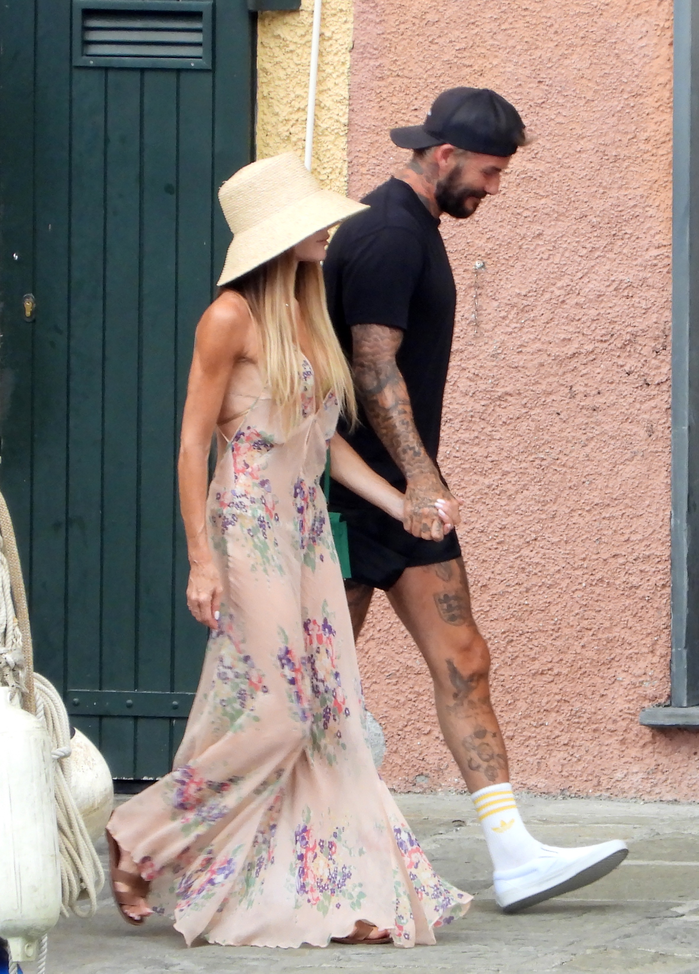 Victoria walks down the street holding hands with David Beckham wearing a sheer floral maxi dress with brown sandals.