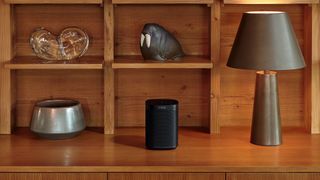 Sonos One SL smart speaker next to a lamp on a shelf