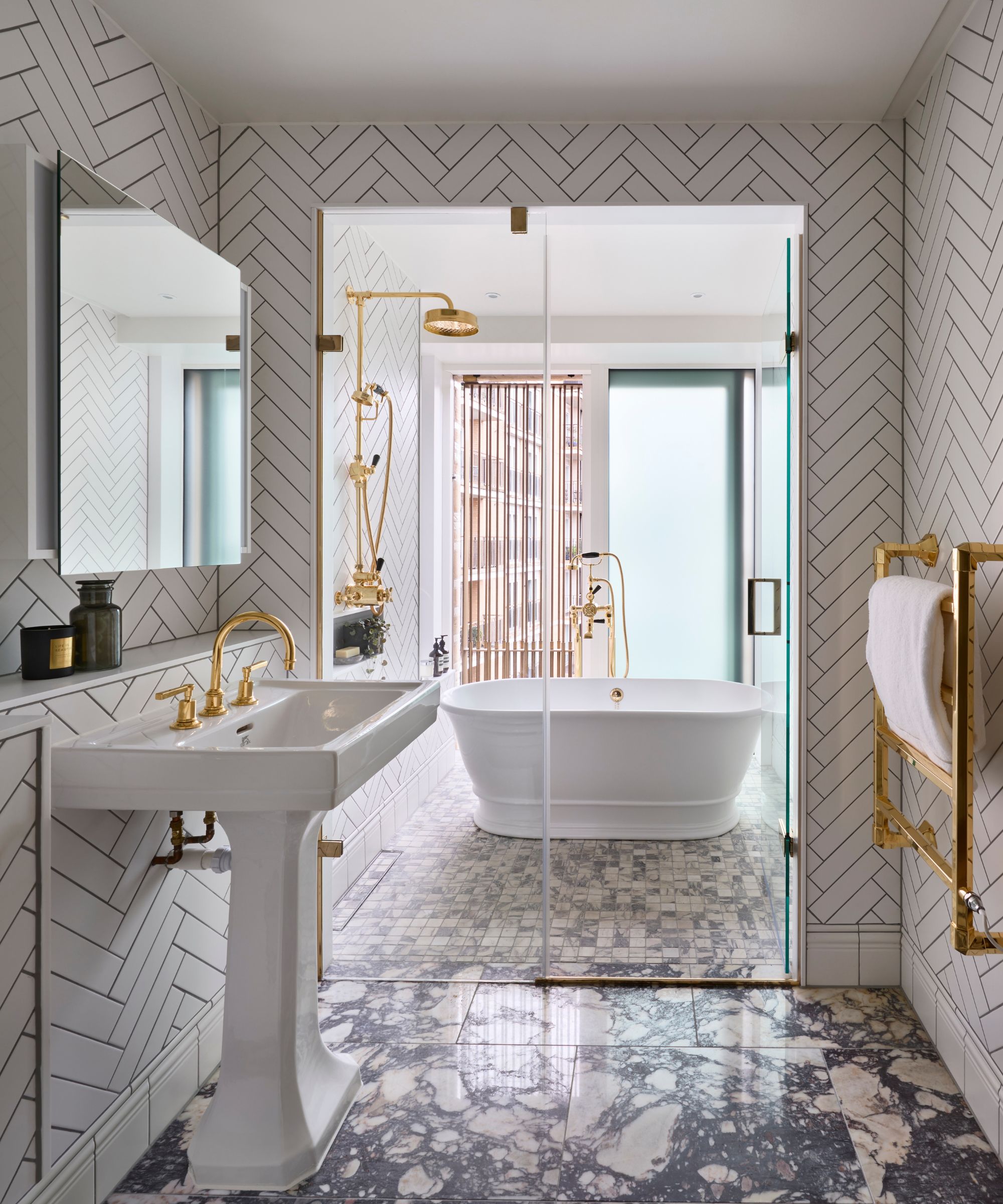 A minimalist bathroom with chevron wall tiles, white sink, white bath and gold hardware