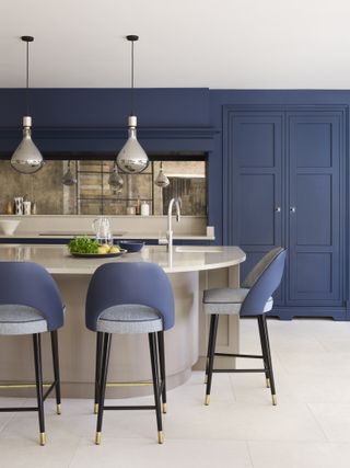 Kitchen with blue cabinets, neutral island with bar stools, mirror backsplash, and stone floor