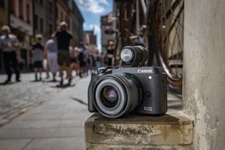 The Canon EOS M6 Mark II, one of the best Canon cameras, with its optional viewfinder sitting on a wall in a street