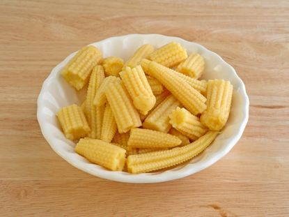 A small white bowl full of baby corn