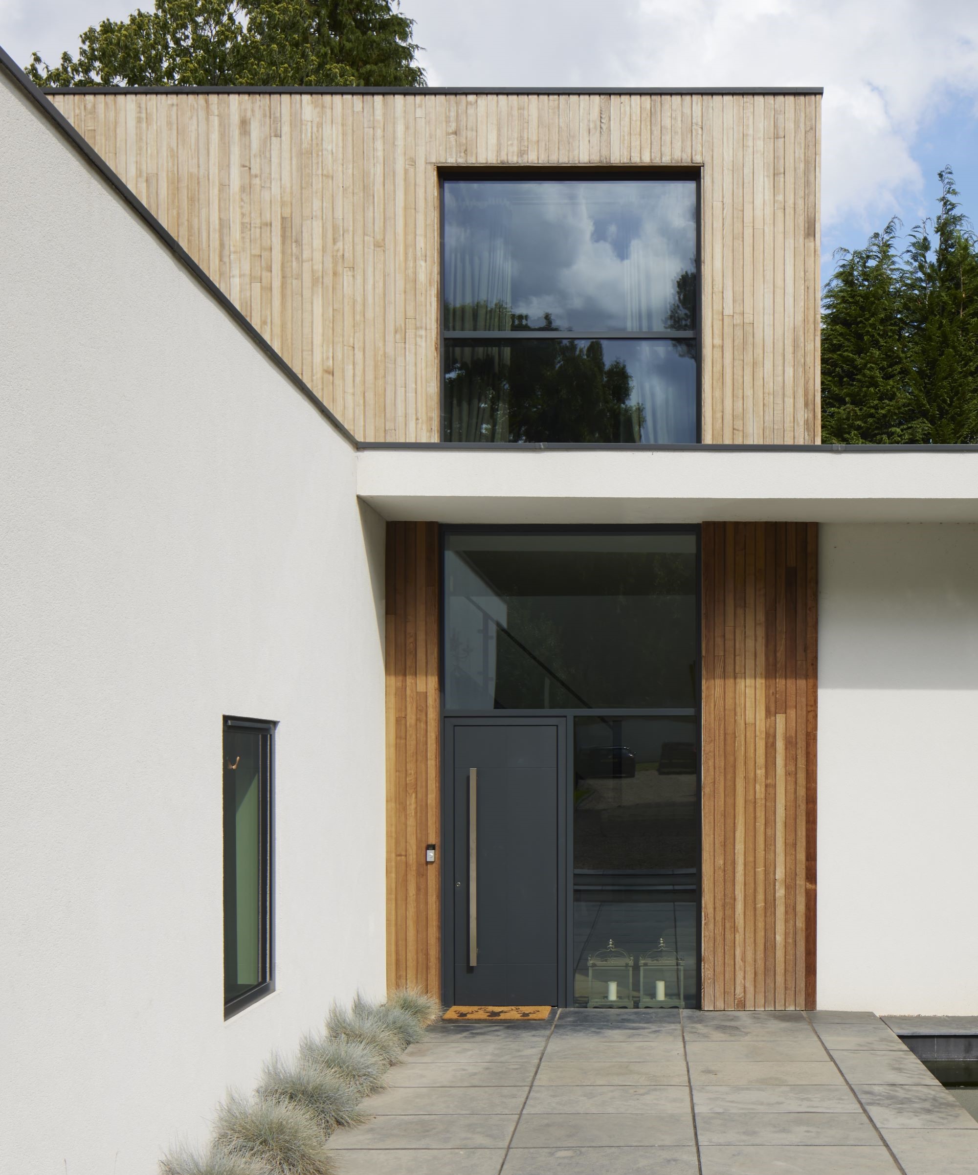 A rendered self build home with vertical larch cladding and a large glass entrance