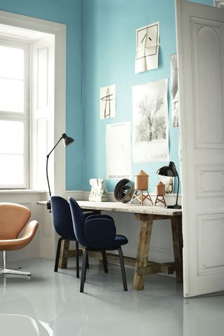 office with a blue wall and white floor, and a large natural wood desk with small blue desk chairs