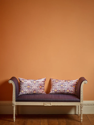 An ornate purple sofa sits in front of a bright burnt orange wall