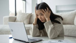 Woman with her head in her hands, looking frustrated, sitting at her laptop