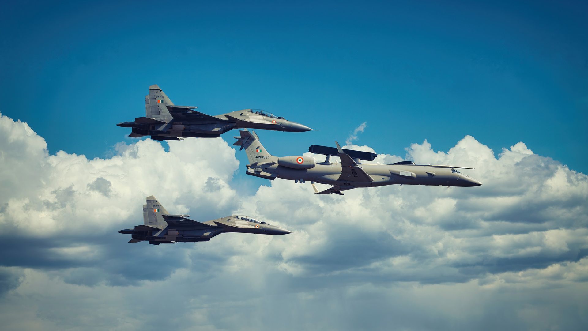 Three gray fighter jets float amidst clouds in the sky.