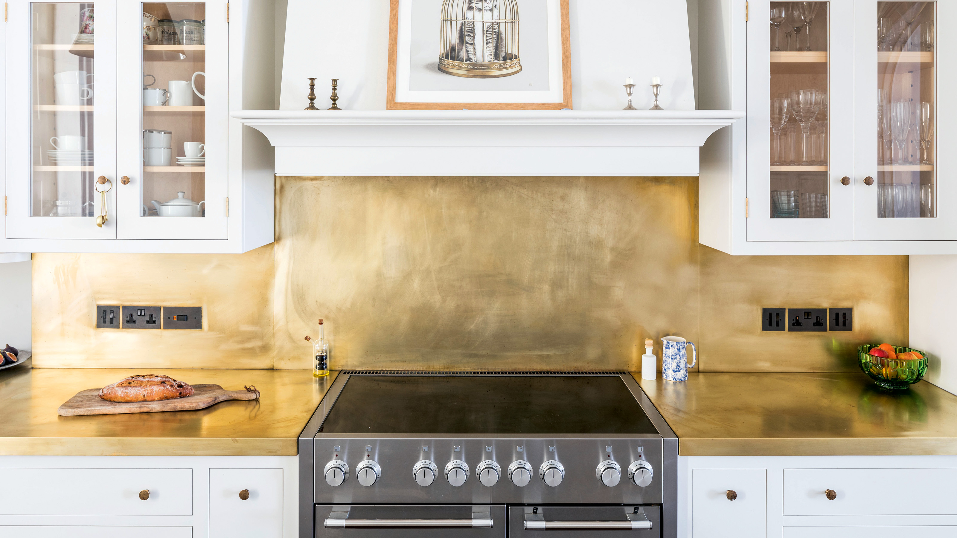 brass splashback above a grey oven with induction hob in white kitchen