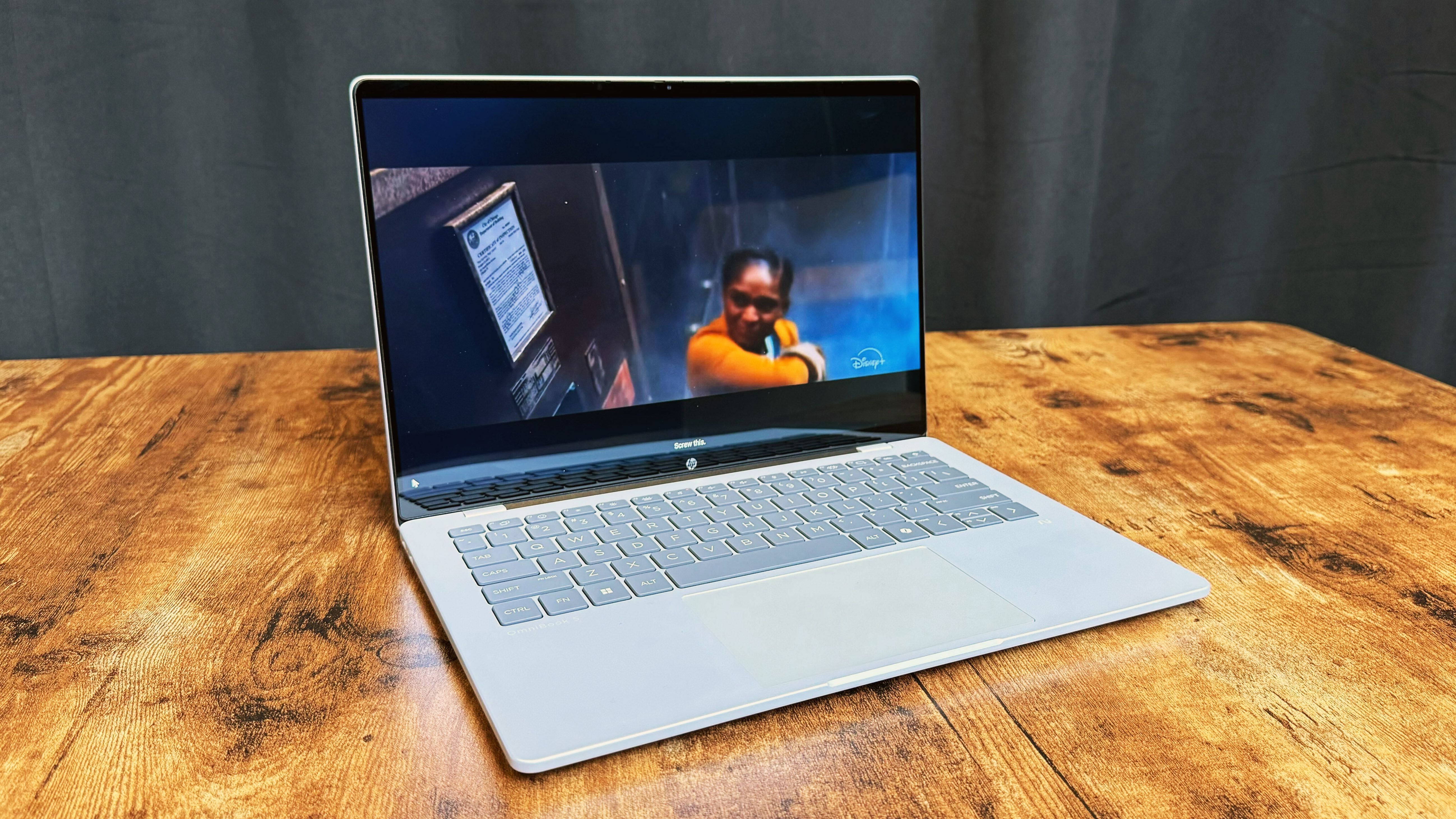 HP OmniBook 5 14 AI PC on a wooden table against a black backdrop.