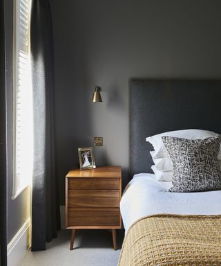 A grey bedroom idea with dark walls, warm wood side table and ochre throw on bed