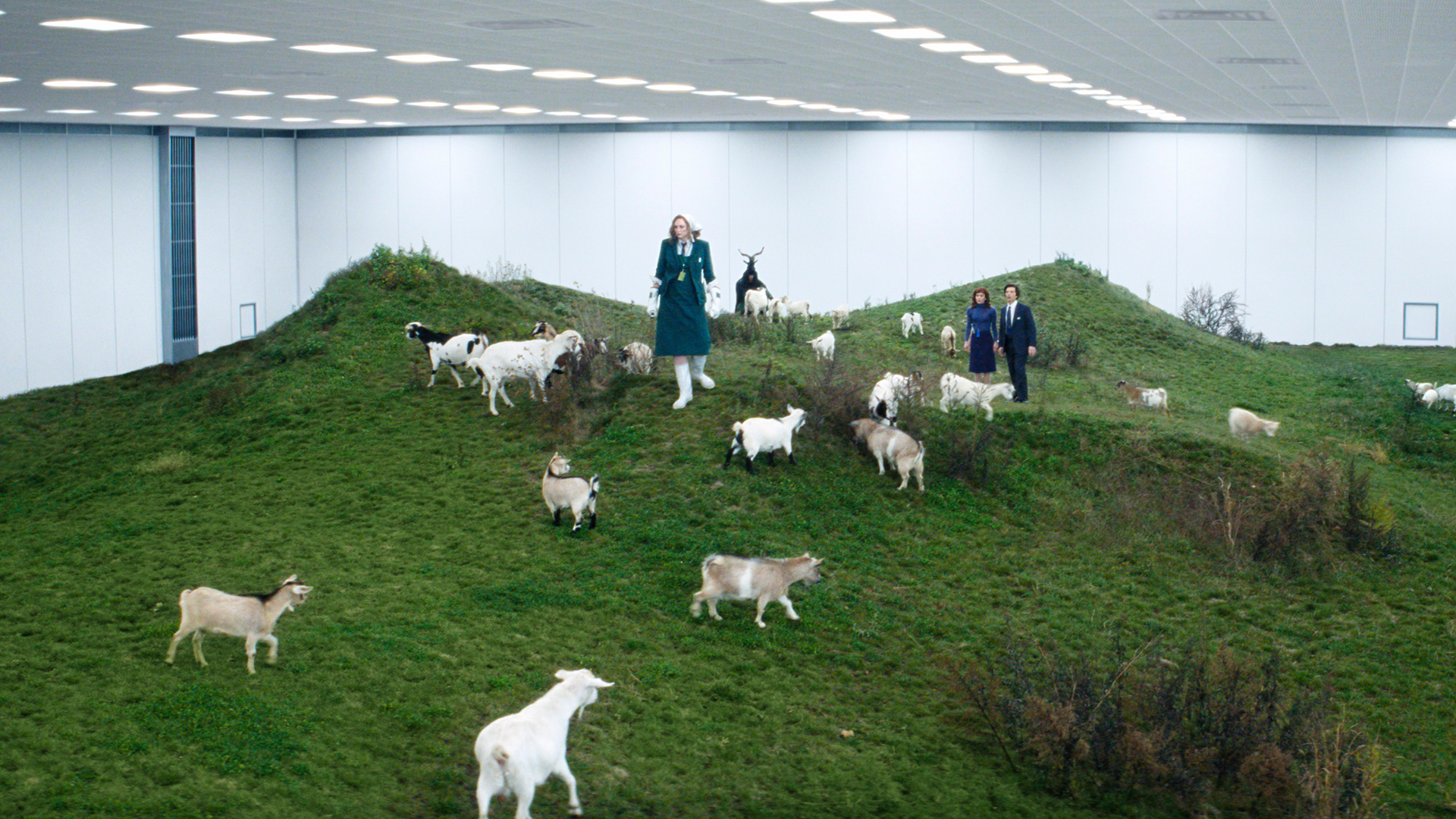 A wide shot of Lorne, Helly, and Mark standing on a fake hill surrounded by goats in Severance season 2 episode 3