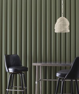 green textured wall with silver table and two black chairs, white pendant light