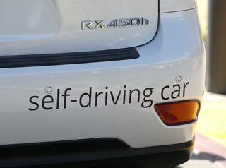 bumper of a white car with the words, "self-driving car"