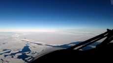 An aerial photograph shows the vast antarctic landscape with a chasm that's filled with blue water.