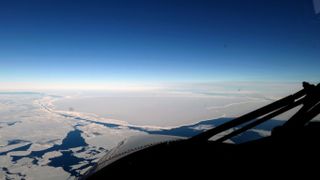 An aerial photograph shows the vast antarctic landscape with a chasm that's filled with blue water.