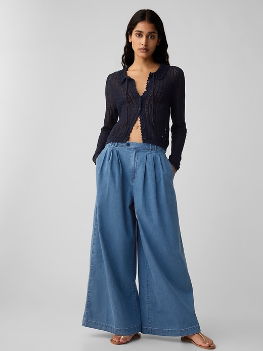 a model wears wide-leg denim trousers with a black cardigan