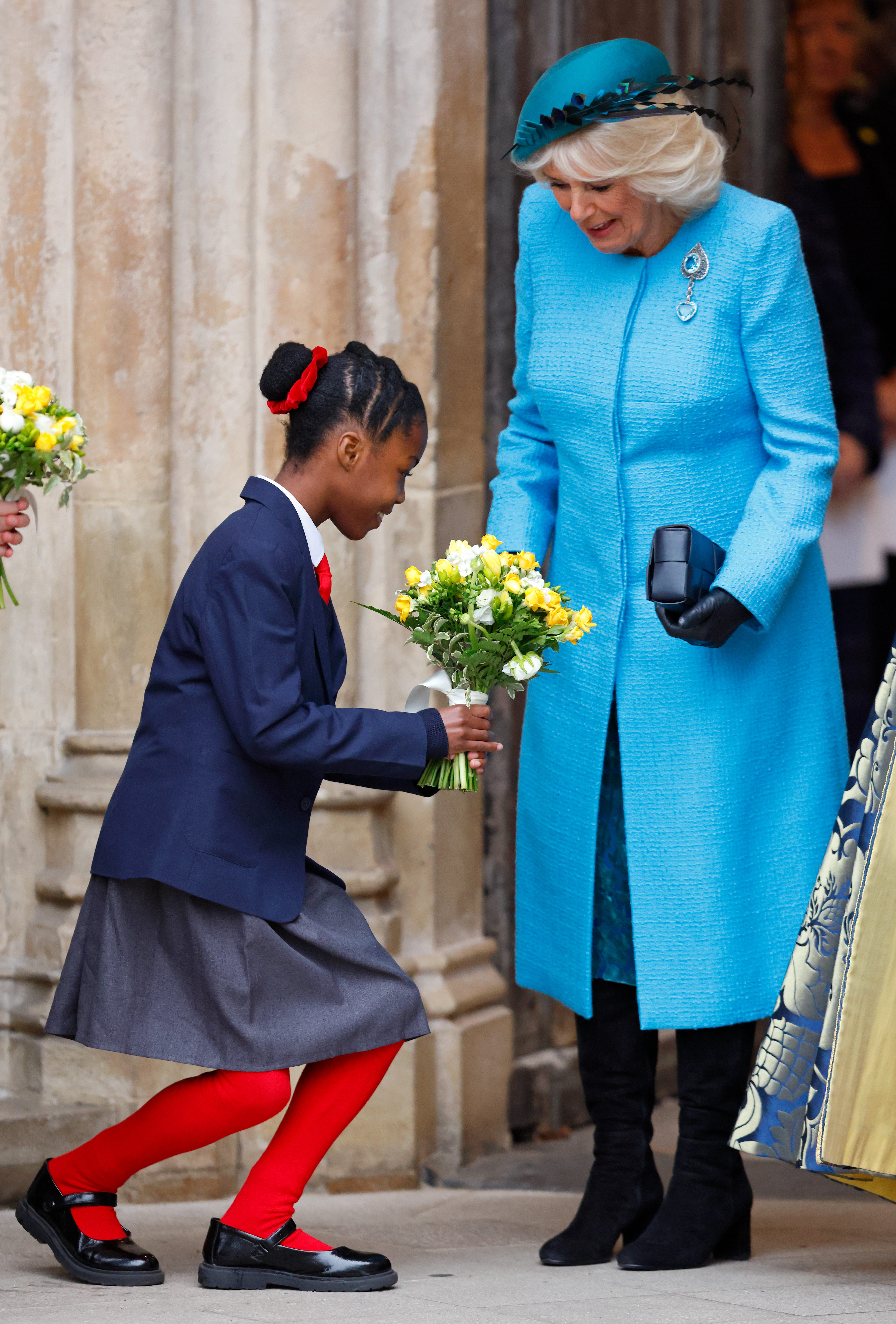 A school girl curtsies to Queen Camilla as she presents her with a bouquet of flowers following the 2024 Commonwealth Day Service at Westminster Abbey on March 11, 2024 in London, England.