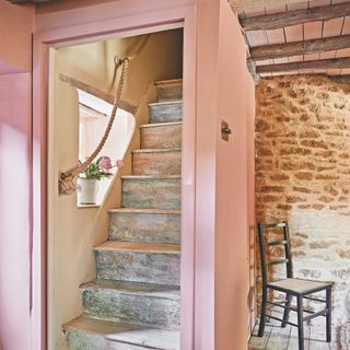 boxed in staircase in small Cotswold cottage with pink painted wood panelling and stone walls