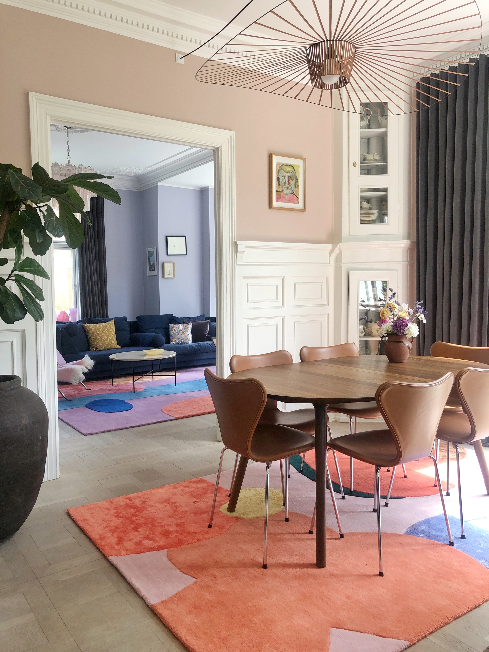 colourful dining room with pink walls, moldings, colorful rugs, and pendant light over timber dining table