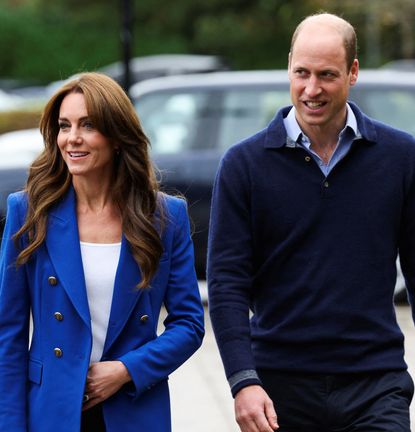 Kate Middleton wearing a blue blazer and Prince William wearing a blue sweater walking through a parking lot