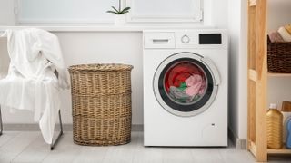 A front load washer running next to a laundry hamper