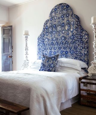 blue and white patterned scalloped edge tall headboard, bed with white bedding and tall white candlesticks on bedside table