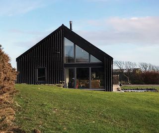 exterior shot of eco house with pitched roof, black cladding and a series of large windows on one half of gable end