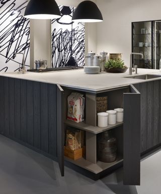 Kitchen cupboard storage ideas integrated into a dark gray island with an L-shaped cupboard on its corner and white countertops.