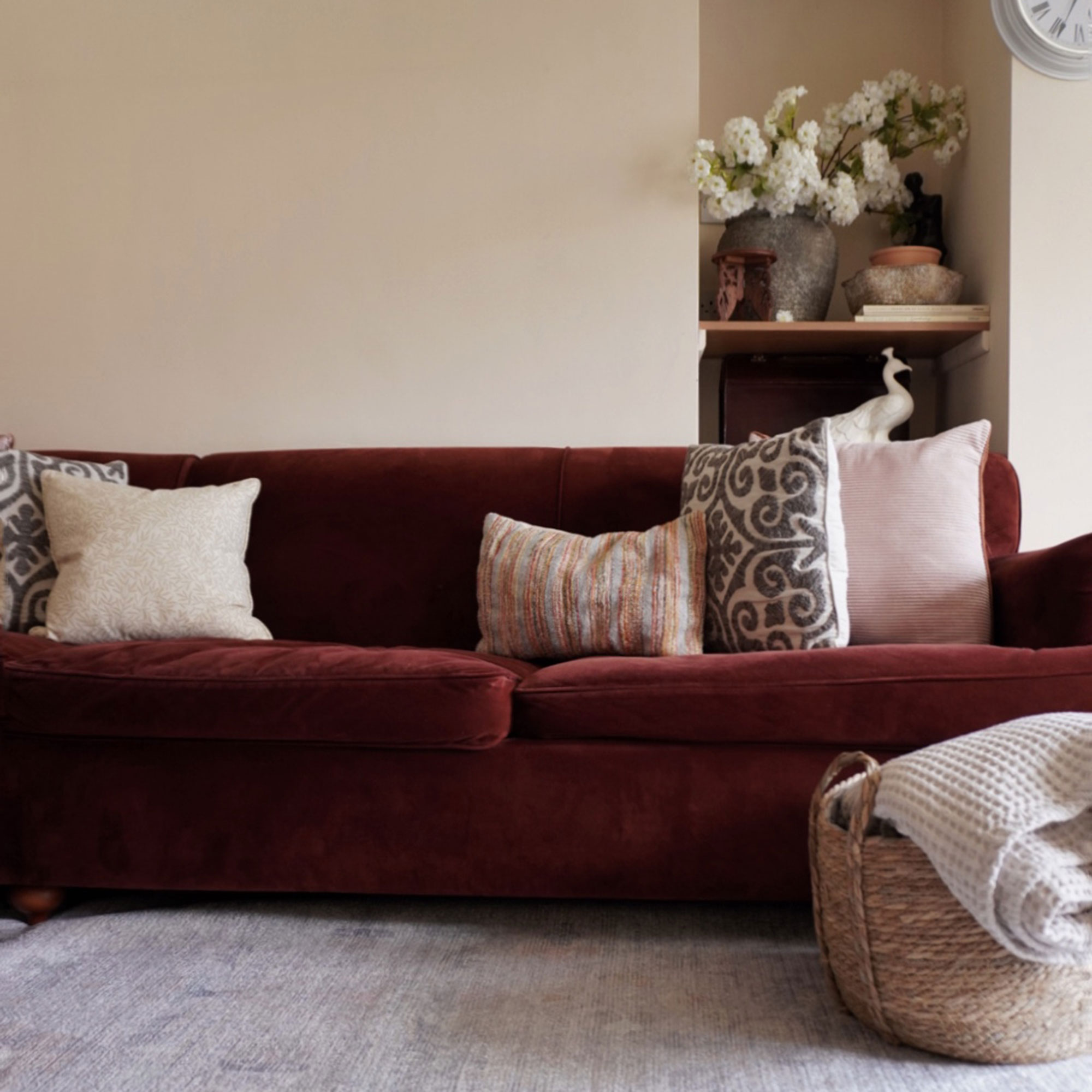 Red velvet sofa with mix-and-match cushions beside basket of throws