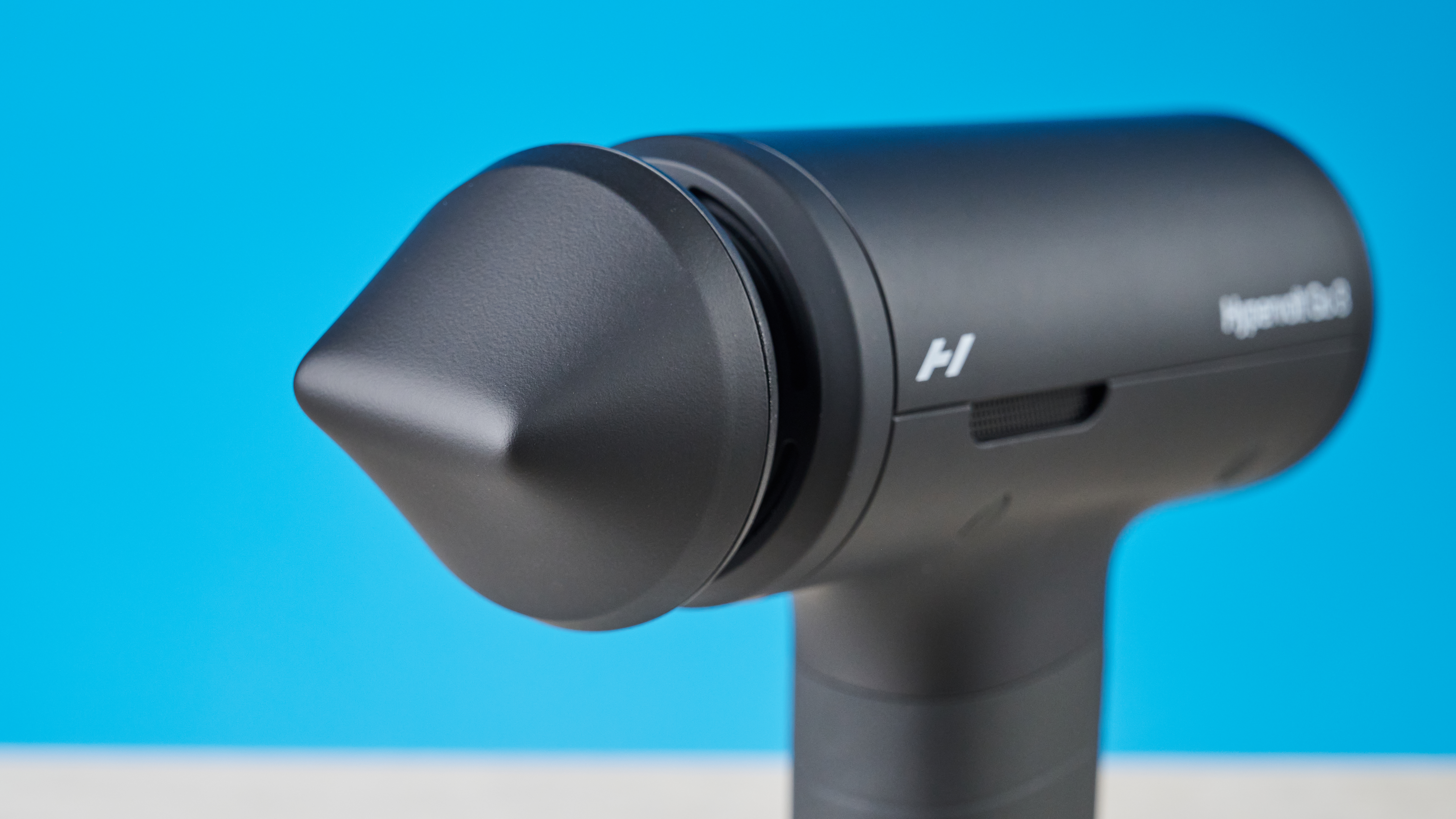 Hyperice Hypervolt Go 3 massage gun photographed in front of a blue background