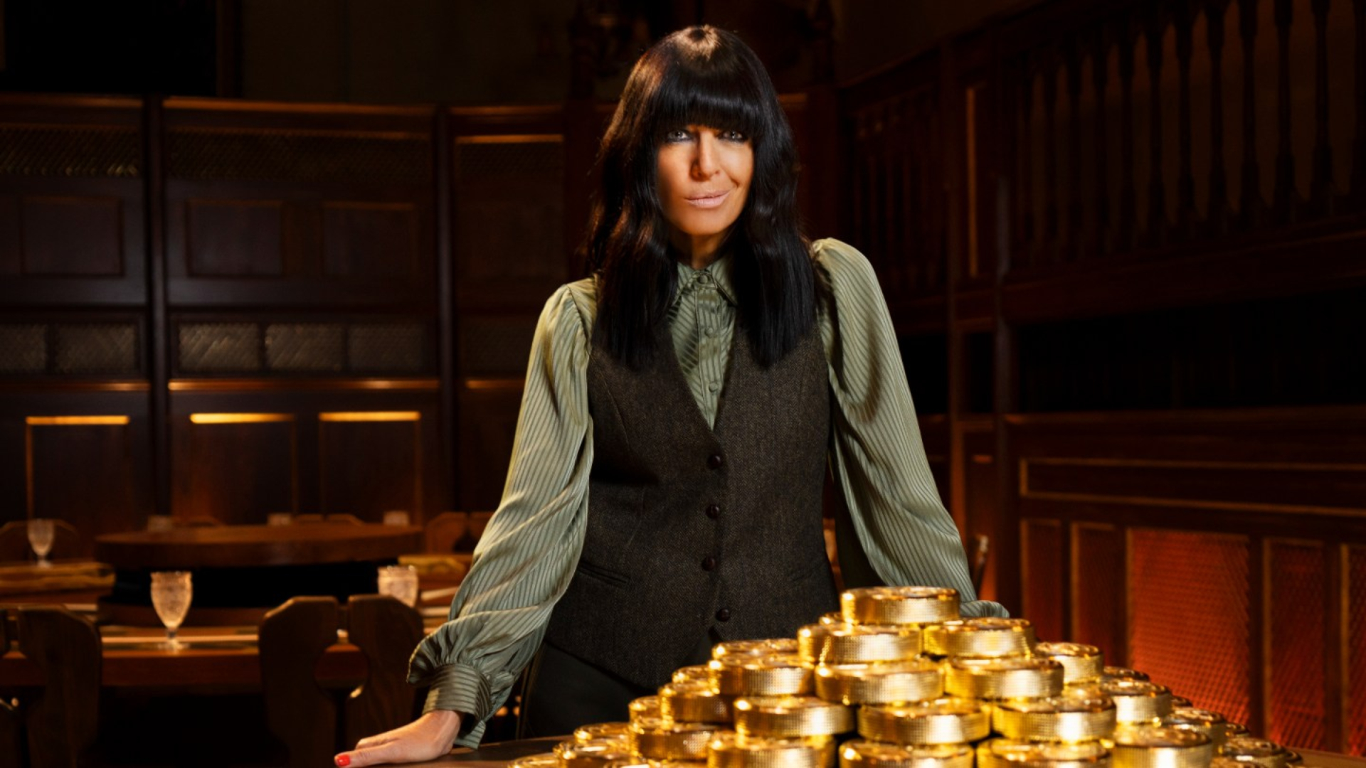 'The Traitors UK' host Claudia Winkleman stands in front of a stack on large gold coins.