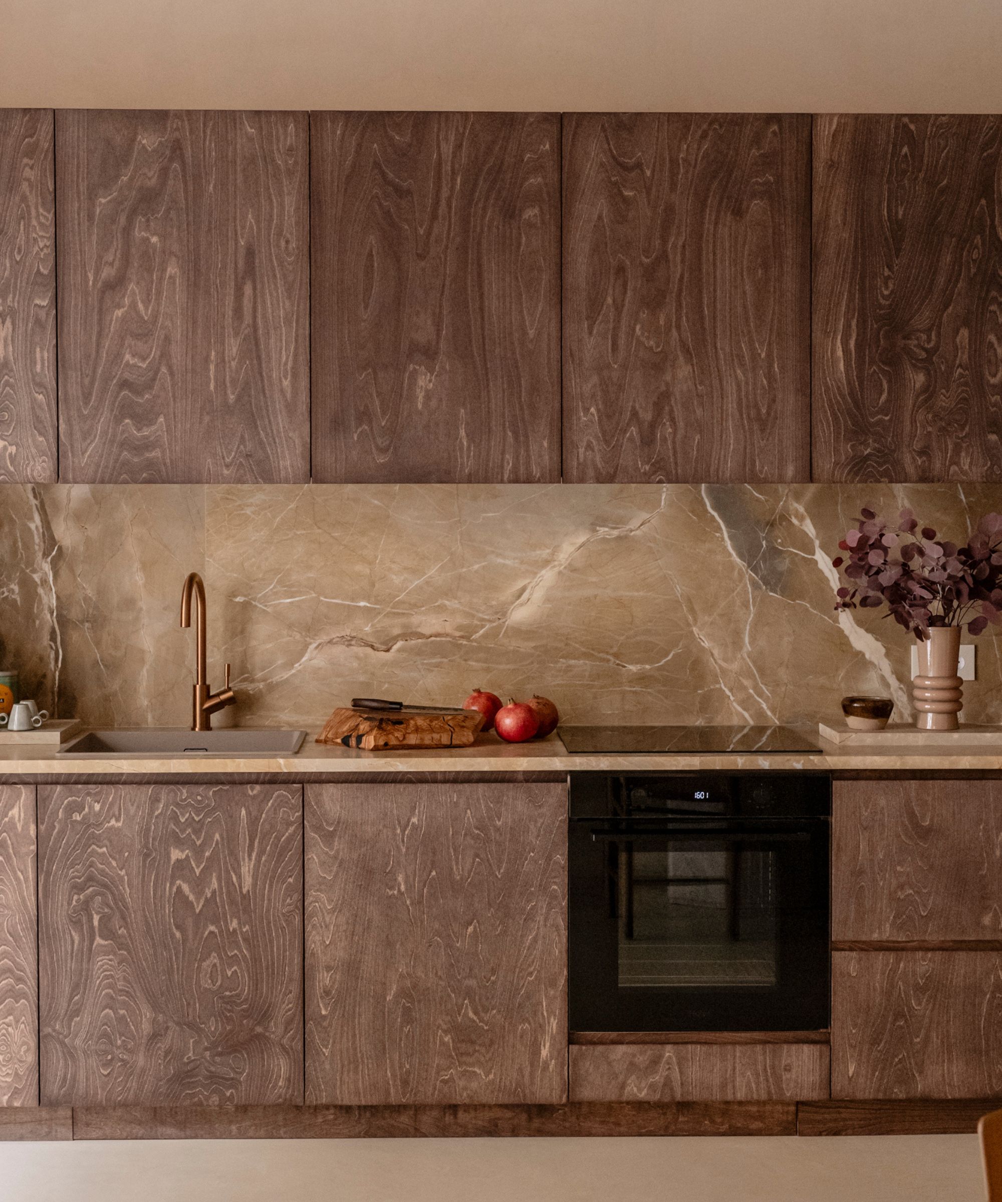 Sophisticated kitchen featuring dark-stained wood grain cabinets paired with a seamless tan marble backsplash and countertop.