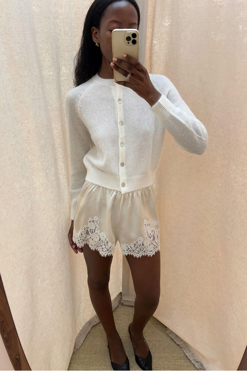 a woman wearing a white knit cardigan and white lace-trim shorts
