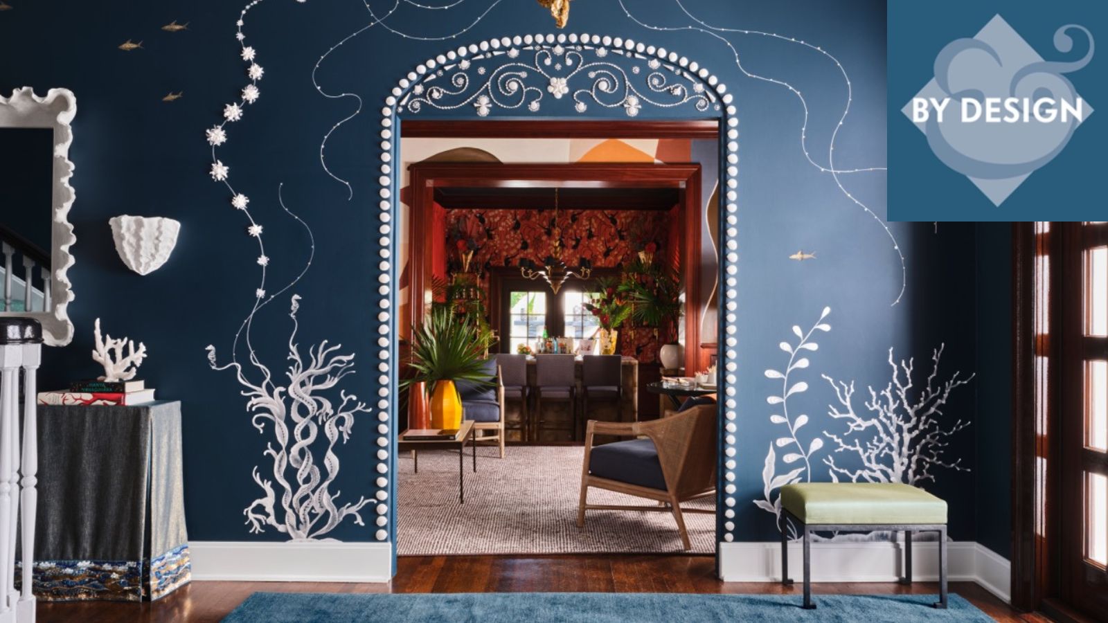Blue entryway with blue painted walls and white flower murals, looking through and arch doorway into a orange living room with furniture and large neutral rug