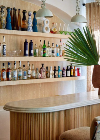 Fluted bamboo bar with a rounded marble top, and shelves lined with bottle behind