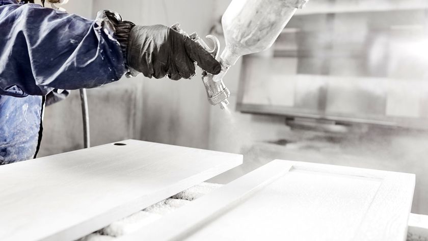 Person in protective gear using an airless sprayer to spray kitchen doors white