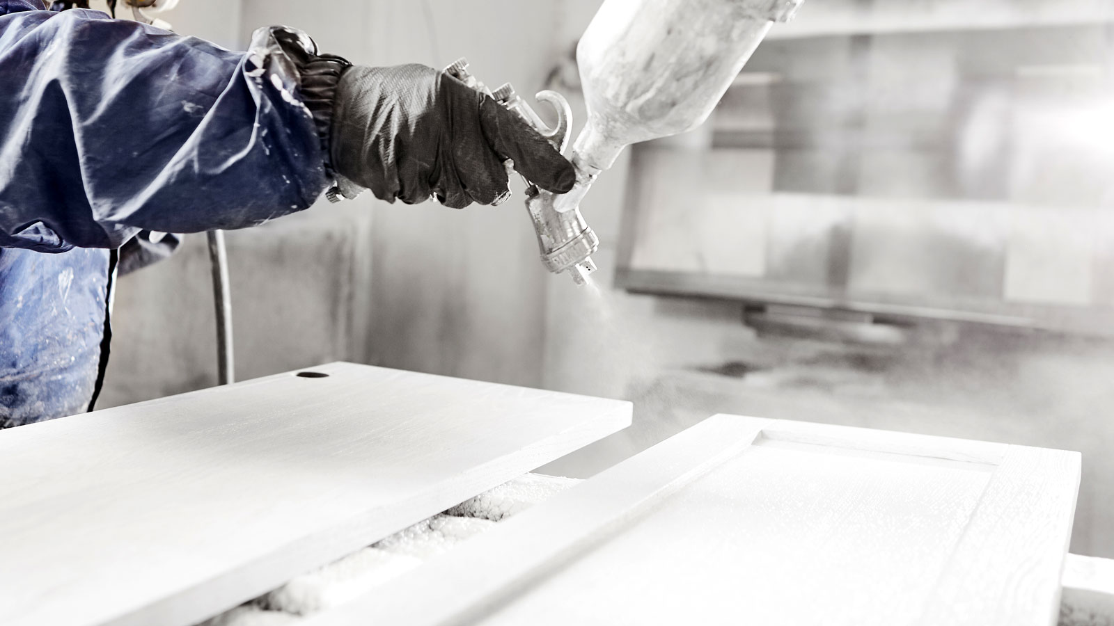 Person in protective gear using an airless sprayer to spray kitchen doors white