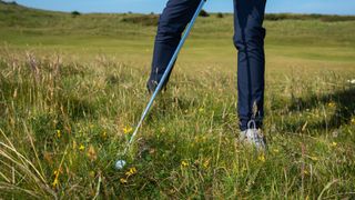 A golfer addressing a golf ball in the rough at Royal Troon