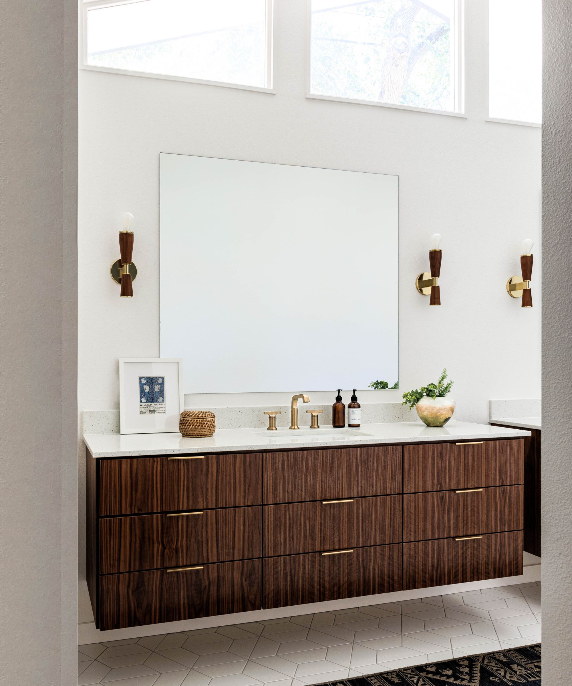 A mid-century modern bathroom with white walls, tall ceilings, a dark wood vanity, and wood and gold wall lights