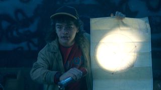 Dustin shining a flashlight at a map he's holding in Stranger Things Season 5