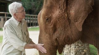 Paul O'Grady in a beige shirt hugs an elephant in Paul O'Grady's Great Elephant Adventure.